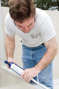 Handyman using a caulking gun to caulk a window.